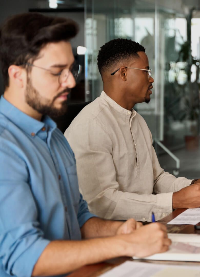 Two focused professionals seated at a conference table taking notes during a meeting-Neutrinos
