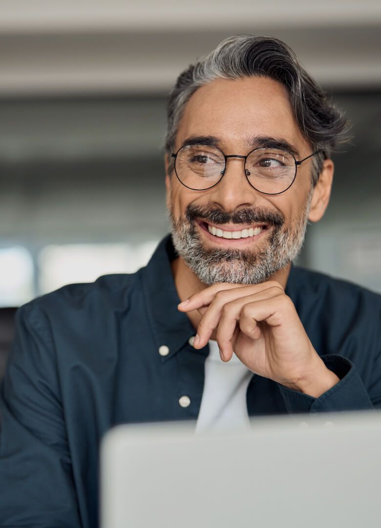 Confident middle-aged man with glasses smiling while working on laptop in office - Neutrinos