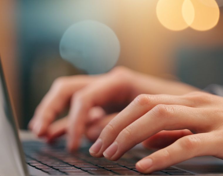 Close-up of hands typing on a laptop keyboard with blurred warm lighting in the background - Neutrinos