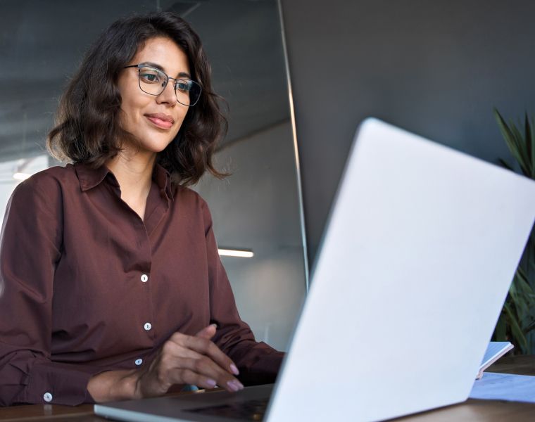 Woman in glasses working on laptop in a modern office setting- Neutrinos