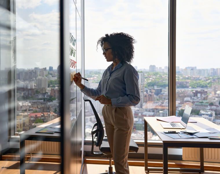 Businesswoman planning on a glass board in a modern office with a city view - Neutrinos