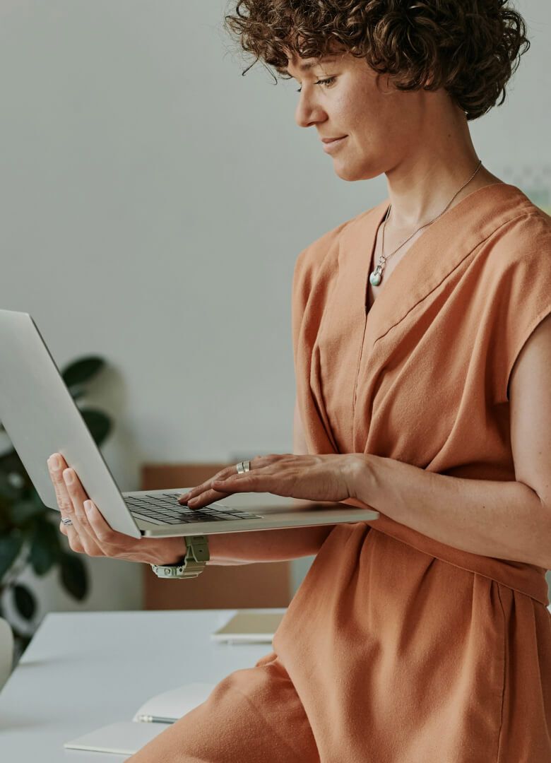 Focused woman in orange dress working on a laptop while seated at the desk in a modern office - Neutrinos