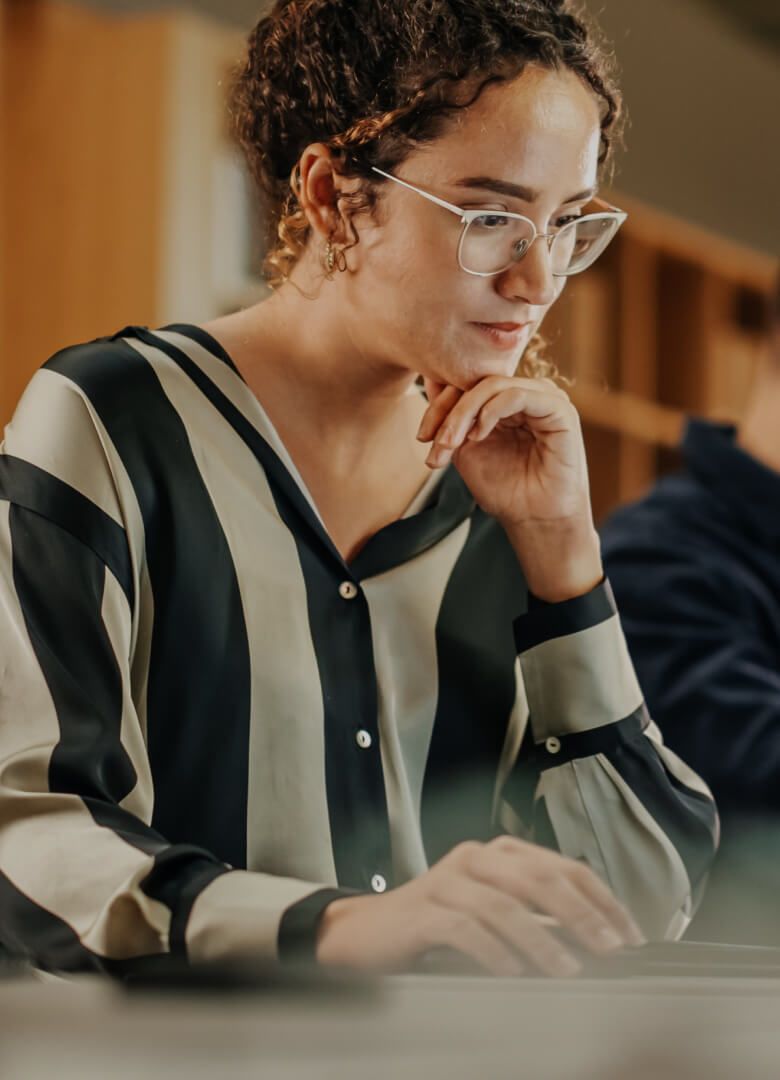 Focused woman working on laptop in modern office environment – Neutrinos